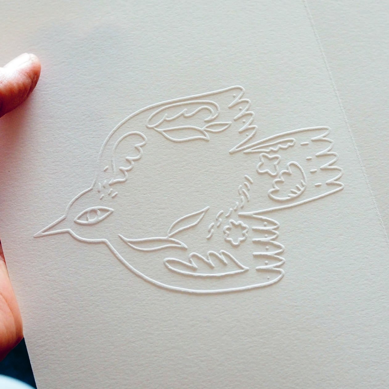 A bird blind-embossed into heavy white paper